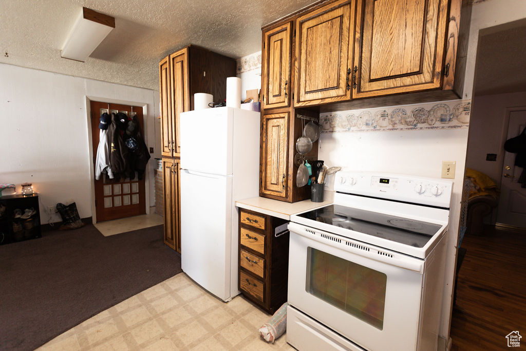 Kitchen with white appliances, brown cabinets, light countertops, a textured ceiling, and light flooring