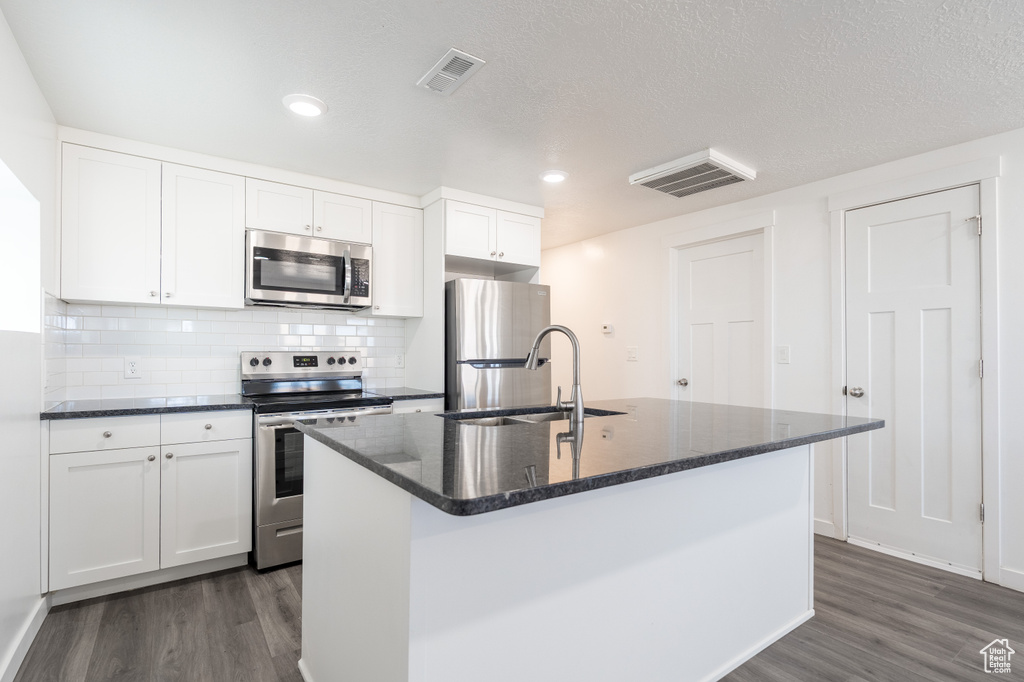 Kitchen with stainless steel appliances, dark wood-style flooring, white cabinets, a center island with sink, and recessed lighting