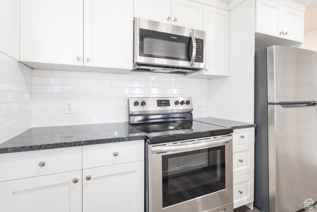 Kitchen featuring stainless steel appliances, white cabinetry, and backsplash