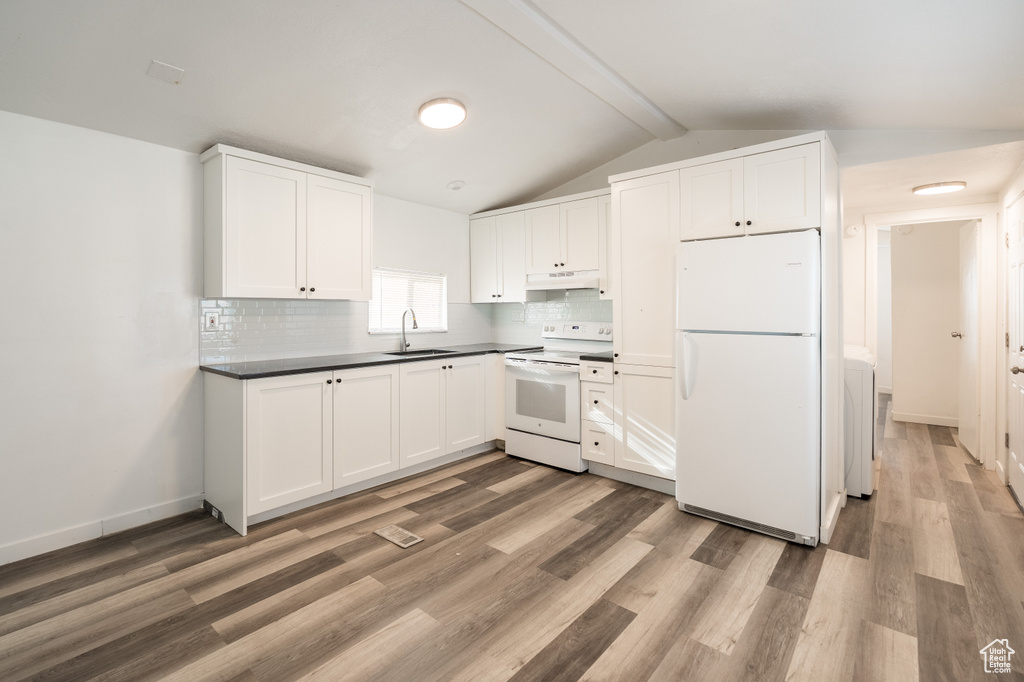 Kitchen with white appliances, under cabinet range hood, dark countertops, light wood-type flooring, and backsplash