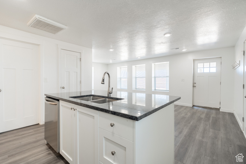 Kitchen featuring a center island with sink, stainless steel dishwasher, dark stone countertops, a textured ceiling, and light wood-type flooring