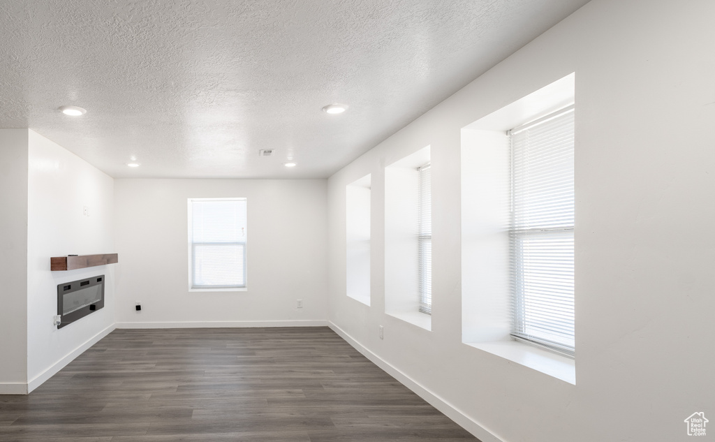 Unfurnished living room with a textured ceiling, heating unit, dark wood-type flooring, a glass covered fireplace, and recessed lighting