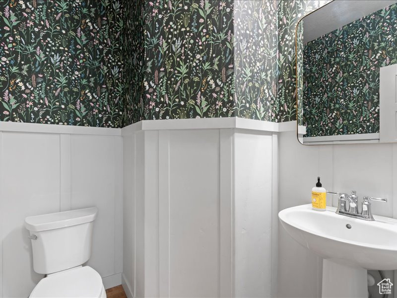 Half bathroom featuring wallpapered walls, wainscoting, and a decorative wall