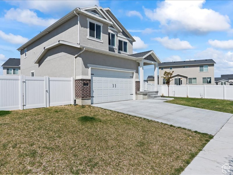 View of front of property featuring a gate, a garage, brick siding, driveway, and stucco siding