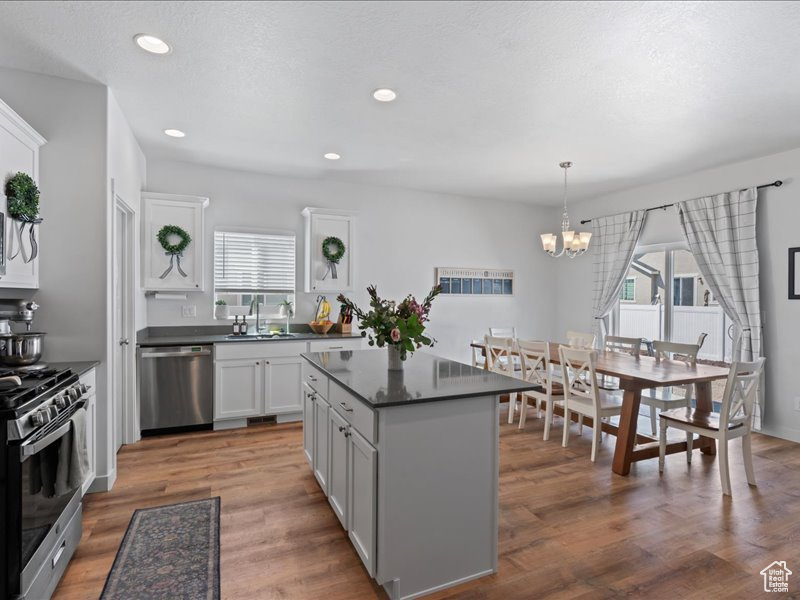 Kitchen with stainless steel appliances, dark countertops, a chandelier, a kitchen island, and white cabinetry