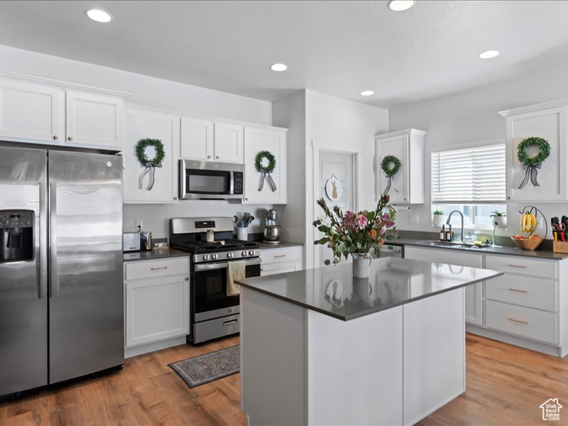 Kitchen with stainless steel appliances, dark countertops, white cabinetry, recessed lighting, and light wood-type flooring