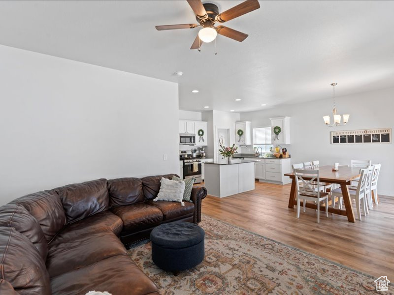 Living room with a chandelier, ceiling fan, light wood-type flooring, and recessed lighting