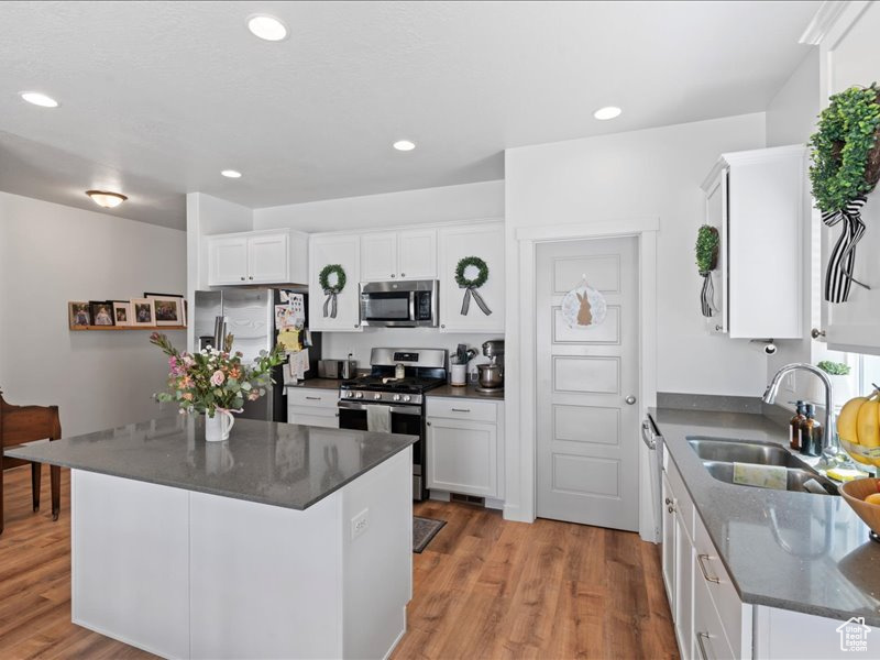Kitchen featuring appliances with stainless steel finishes, wood finished floors, white cabinetry, recessed lighting, and a kitchen island