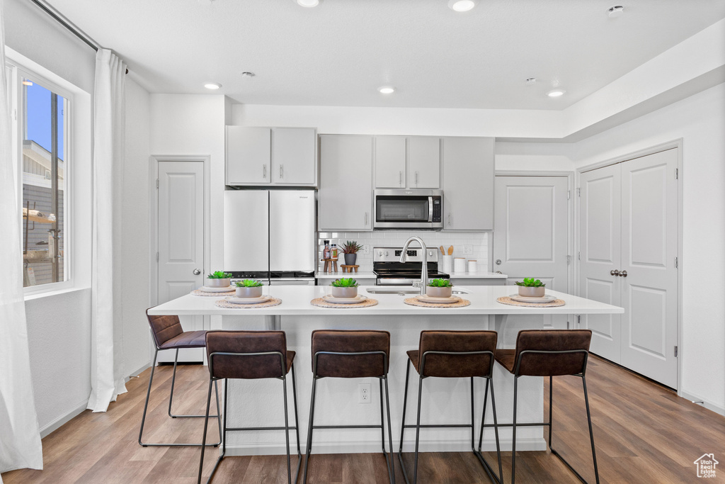Kitchen featuring stainless steel appliances, a breakfast bar area, light countertops, backsplash, and recessed lighting