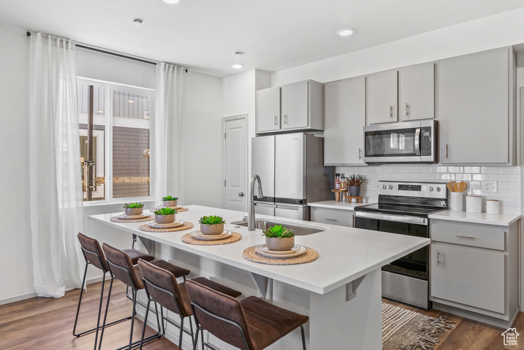 Kitchen with appliances with stainless steel finishes, gray cabinetry, light countertops, backsplash, and wood finished floors