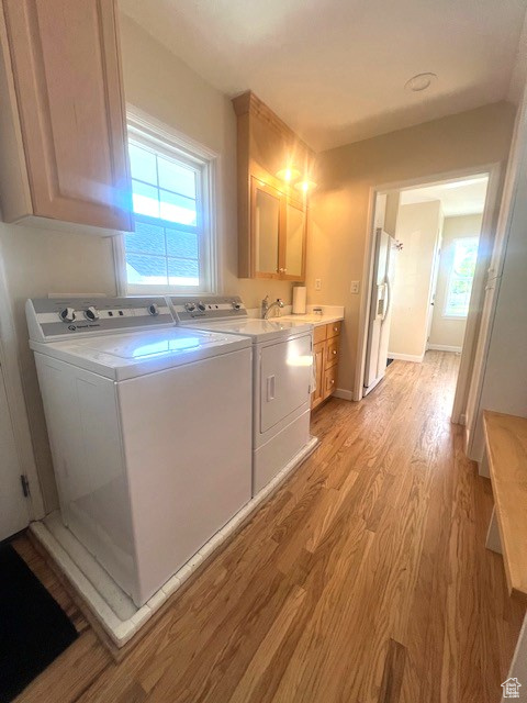 Laundry area featuring separate washer and dryer, cabinet space, and light wood-style floors