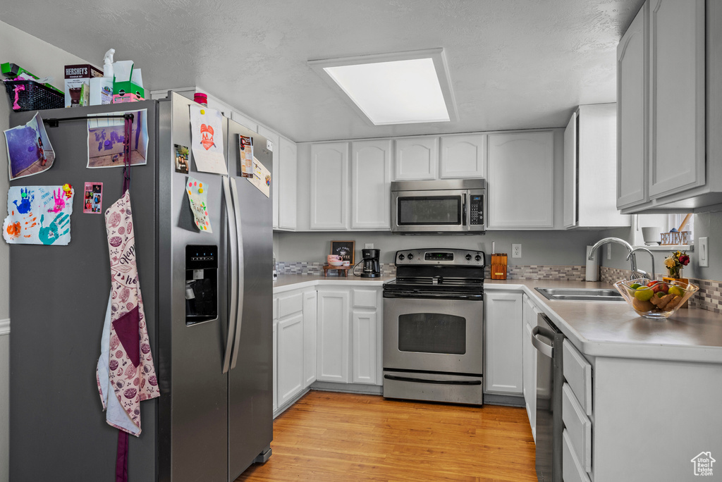 Kitchen with stainless steel appliances, light countertops, light wood finished floors, and white cabinets