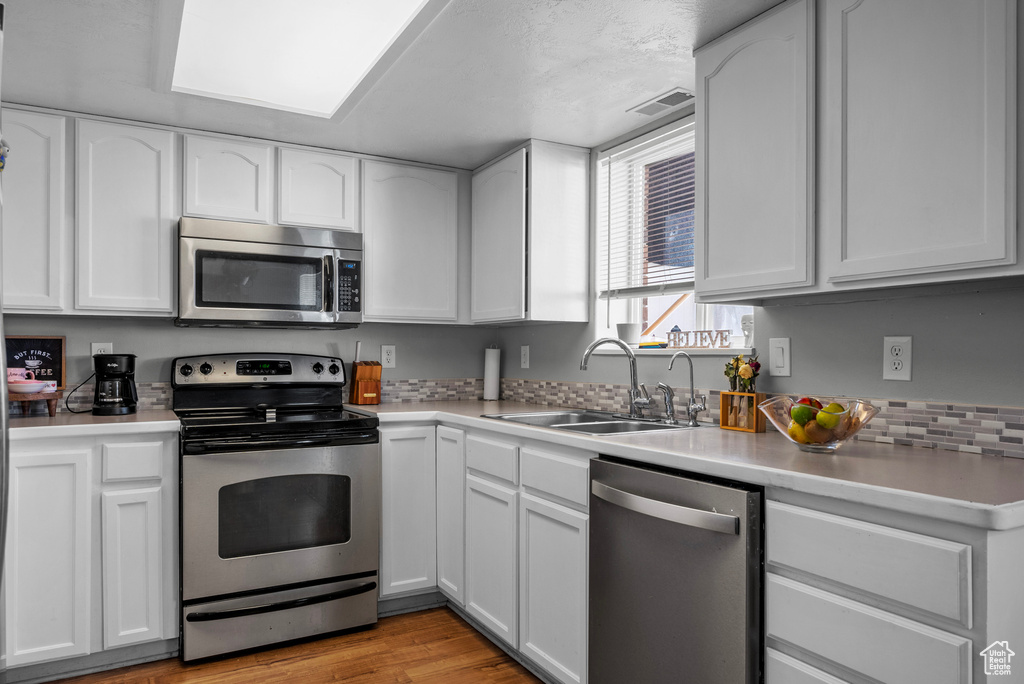 Kitchen with appliances with stainless steel finishes, white cabinetry, light countertops, and light wood finished floors