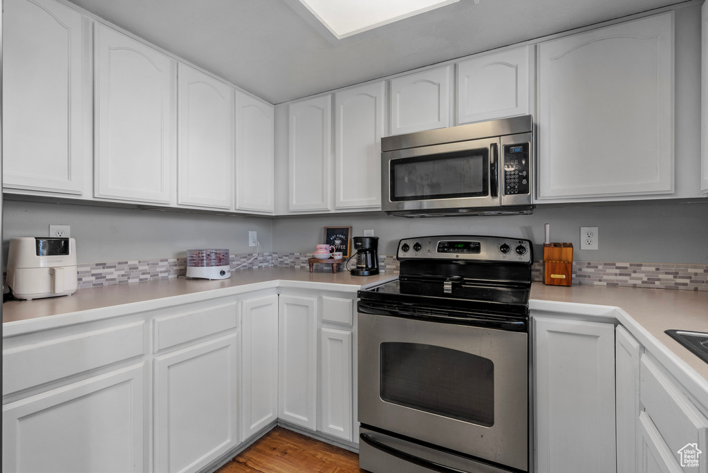 Kitchen with appliances with stainless steel finishes, white cabinets, light countertops, light wood-style flooring, and tasteful backsplash