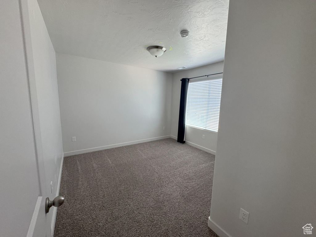 Empty room with carpet floors, a smoke detector, and a textured ceiling
