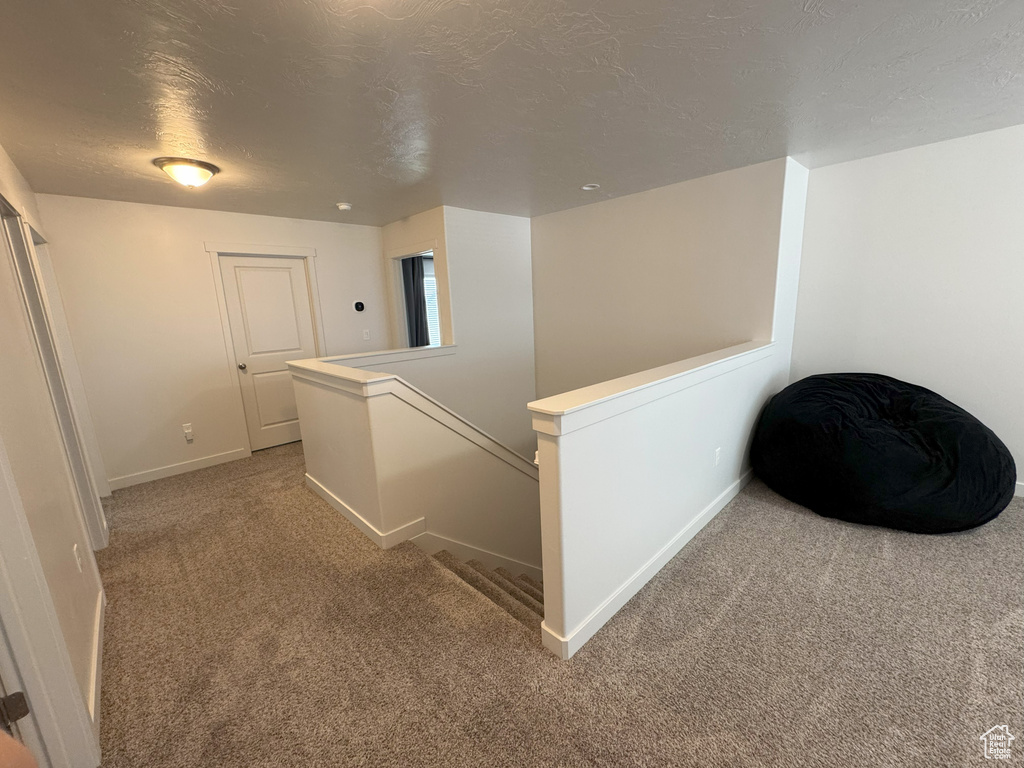Hallway featuring carpet floors, an upstairs landing, and a textured ceiling