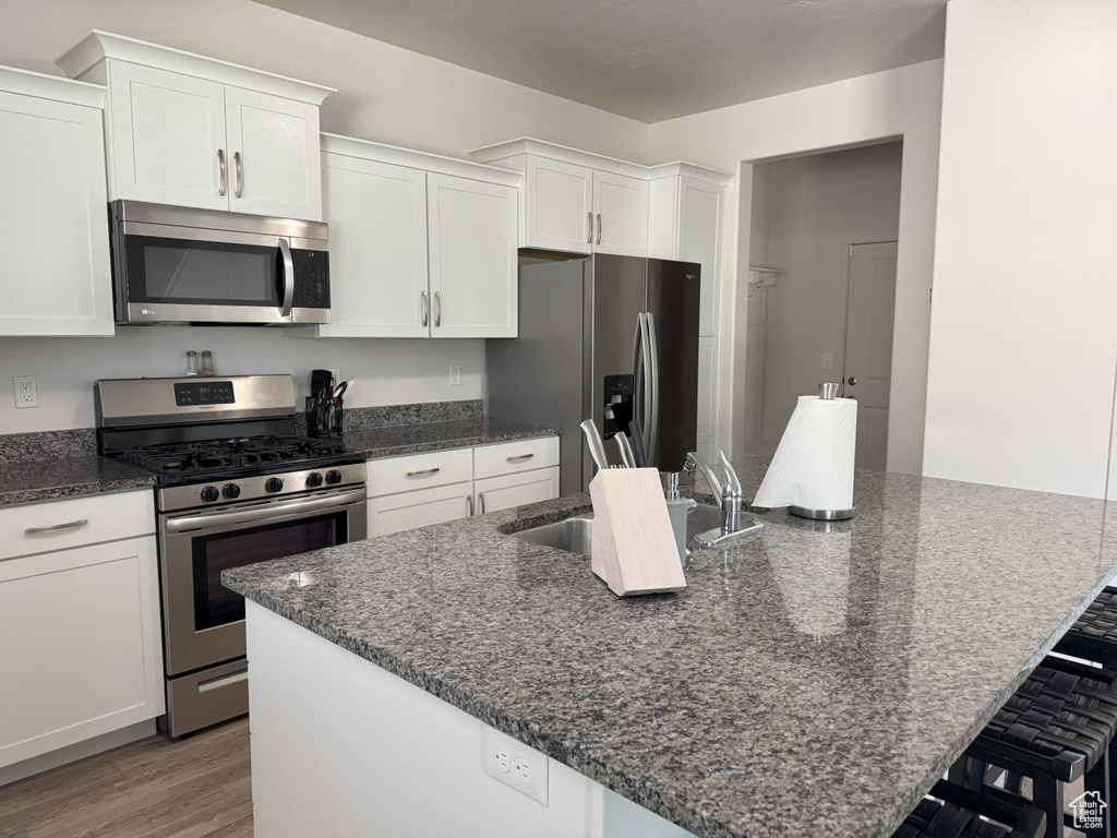 Kitchen with appliances with stainless steel finishes, white cabinets, a large island, and light wood-style floors