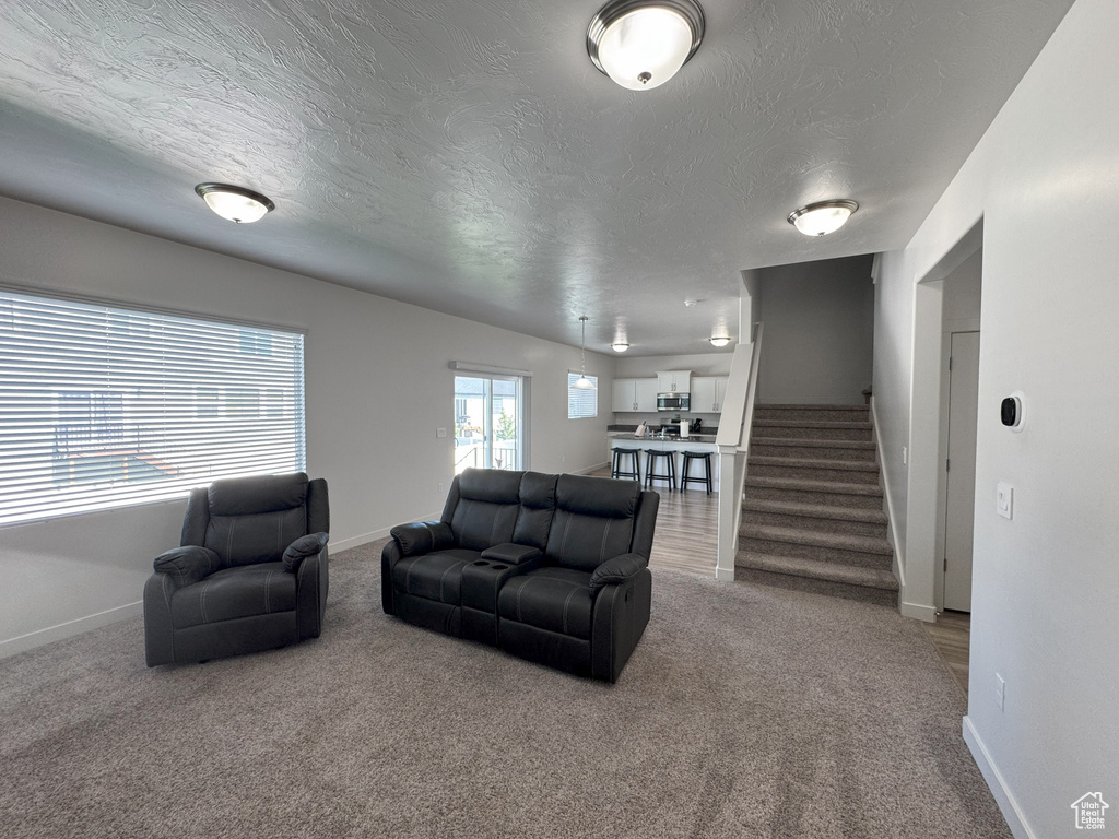 Living area with a textured ceiling, stairway, and carpet flooring