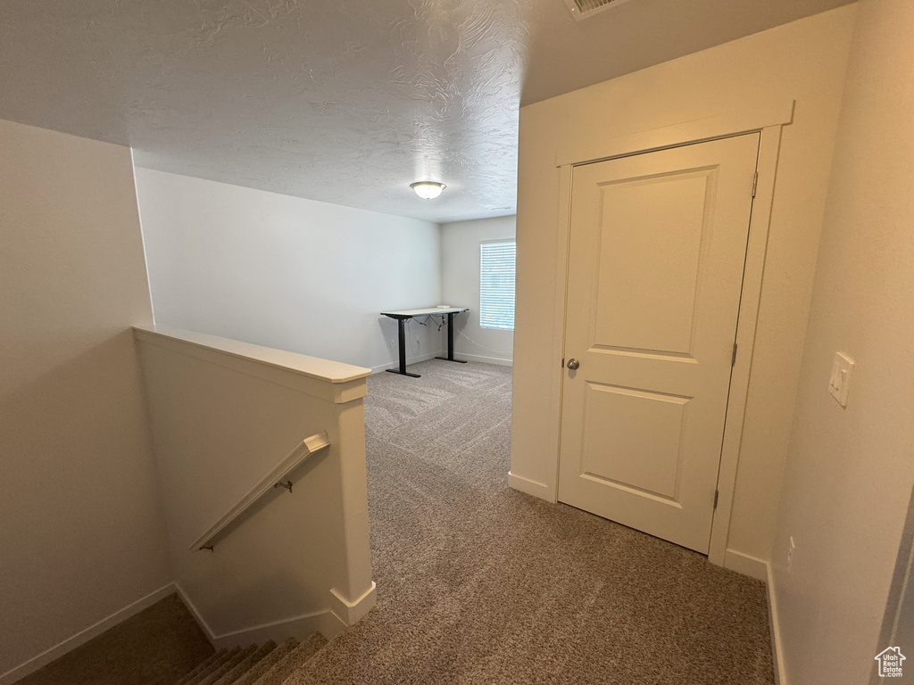 Corridor with an upstairs landing, carpet floors, and a textured ceiling