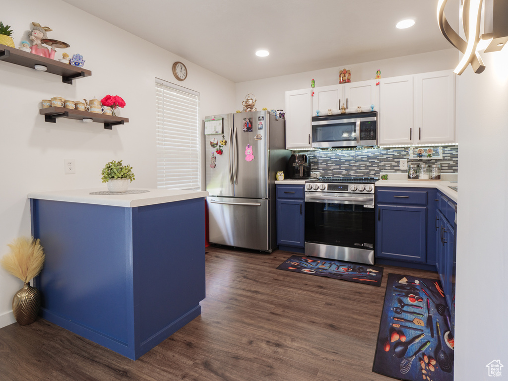 Kitchen featuring appliances with stainless steel finishes, blue cabinets, light countertops, dark wood-type flooring, and tasteful backsplash