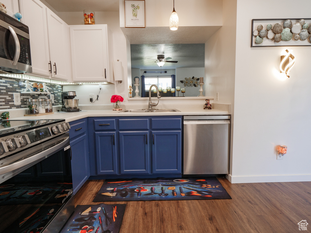 Kitchen with appliances with stainless steel finishes, blue cabinetry, a ceiling fan, dark wood-type flooring, and light countertops