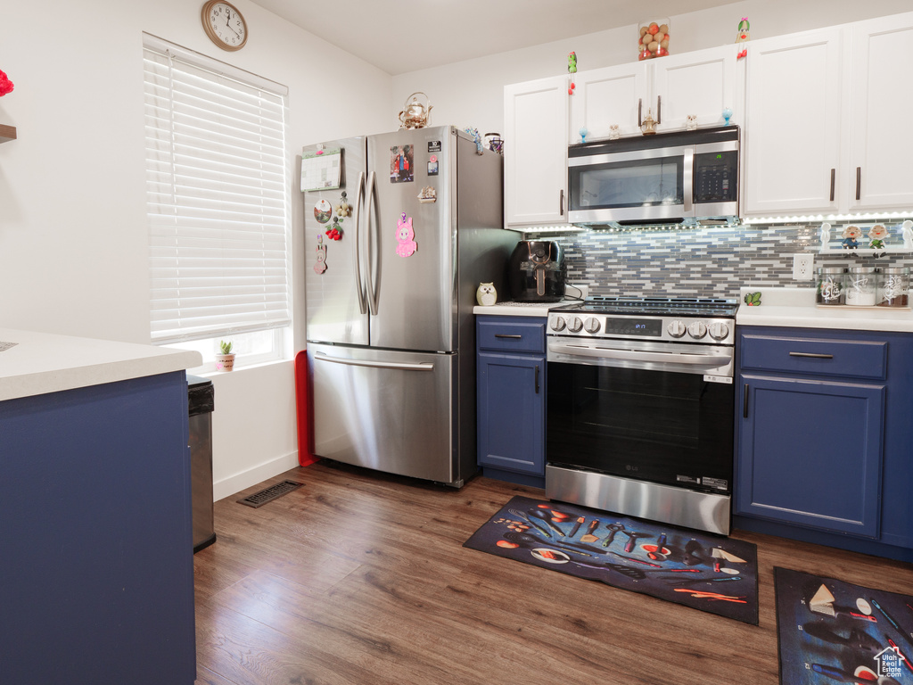 Kitchen with appliances with stainless steel finishes, blue cabinets, light countertops, and dark wood-type flooring