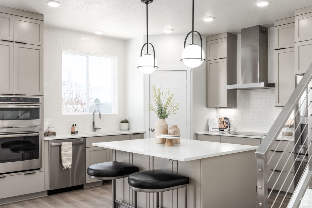 Kitchen featuring wall chimney exhaust hood, appliances with stainless steel finishes, gray cabinets, backsplash, and recessed lighting