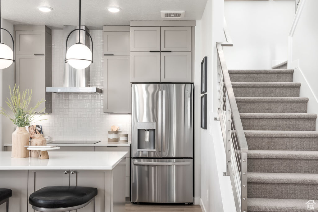 Kitchen with stainless steel refrigerator with ice dispenser, gray cabinets, black electric stovetop, backsplash, and light countertops
