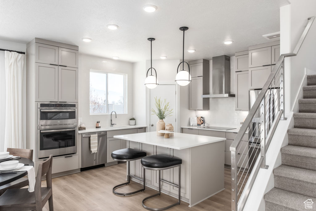 Kitchen featuring stainless steel appliances, wall chimney exhaust hood, gray cabinetry, light wood-style flooring, and recessed lighting