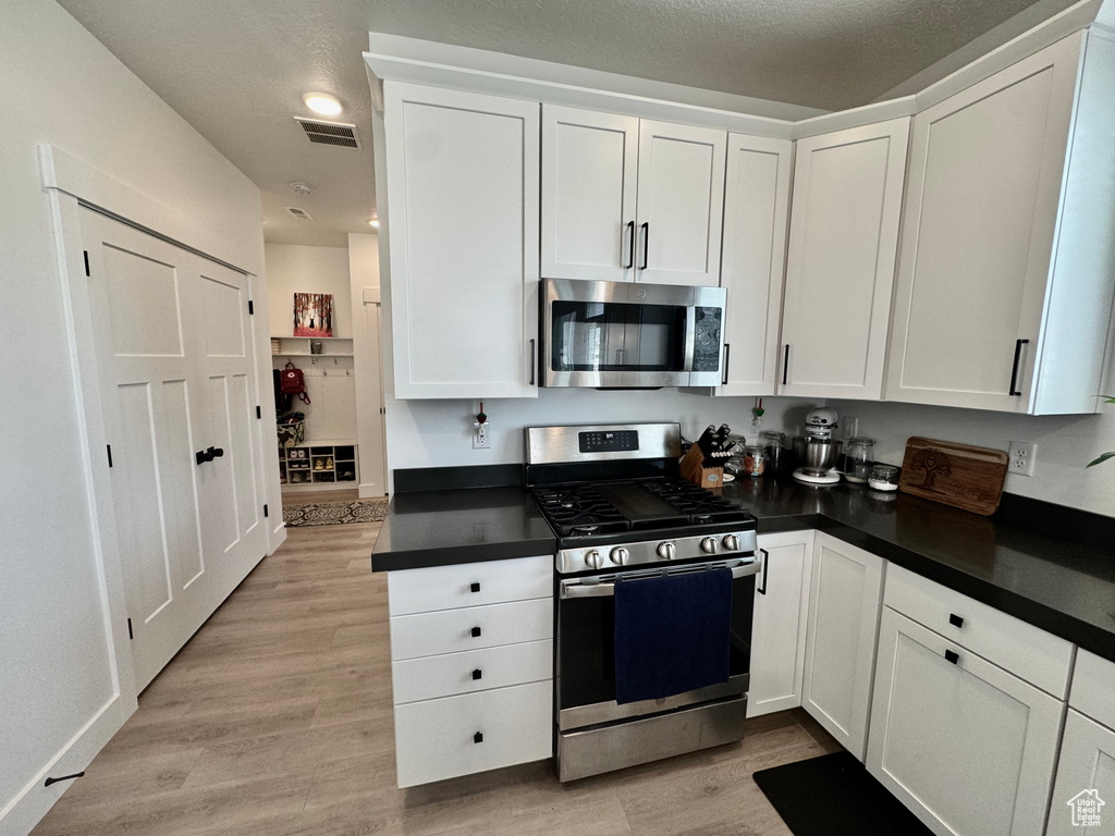 Kitchen with stainless steel appliances, dark countertops, and white cabinetry