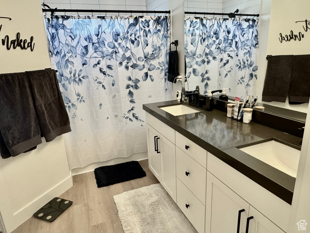 Full bathroom featuring wood finished floors, double vanity, and shower / tub combo with curtain