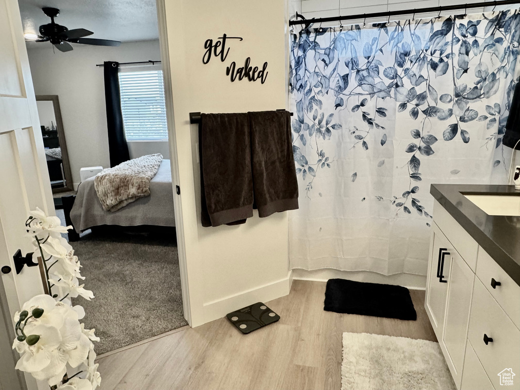 Bathroom featuring ensuite bath, wood finished floors, vanity, shower / bathtub combination with curtain, and a ceiling fan