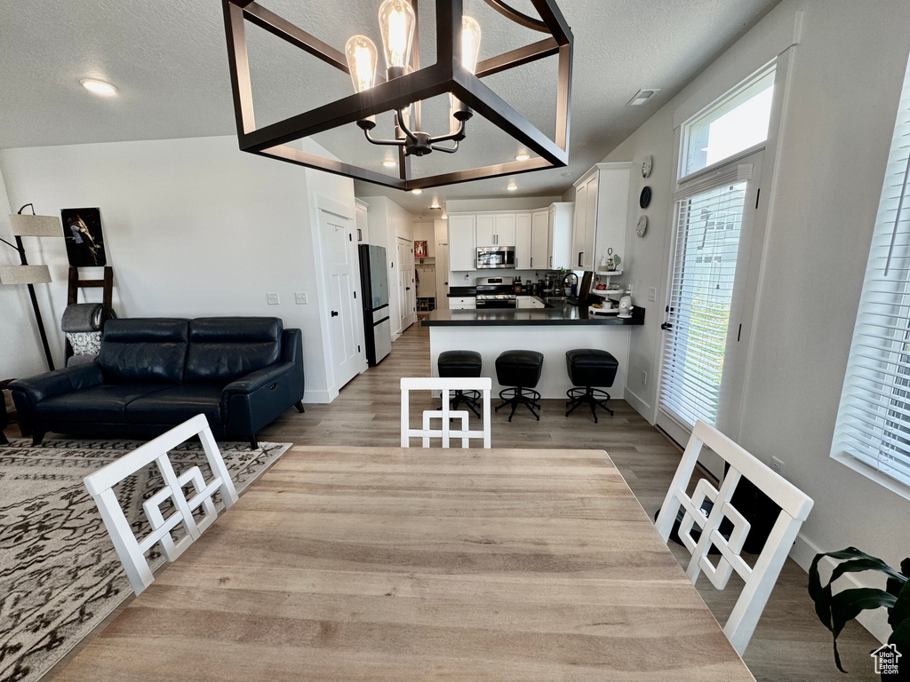 Dining area featuring plenty of natural light, light wood-type flooring, a chandelier, and a textured ceiling