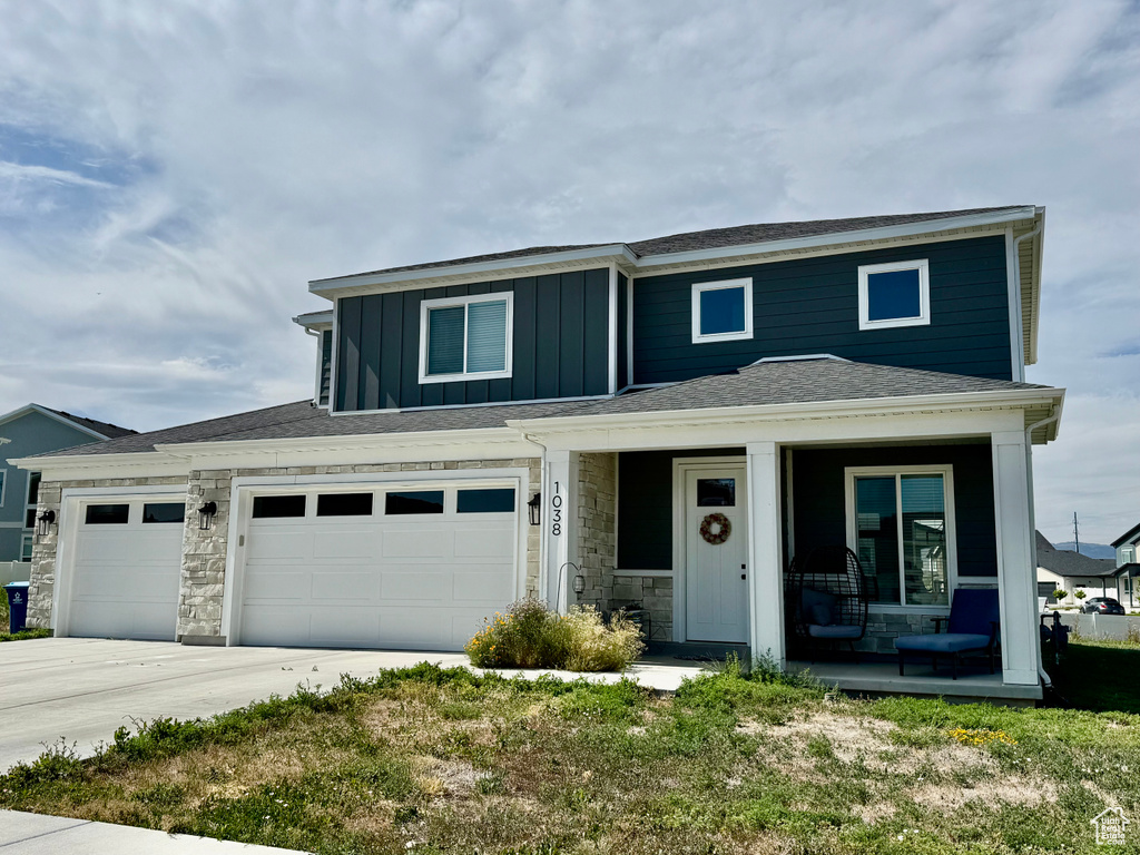 View of front of property featuring covered porch, board and batten siding, stone siding, and concrete driveway