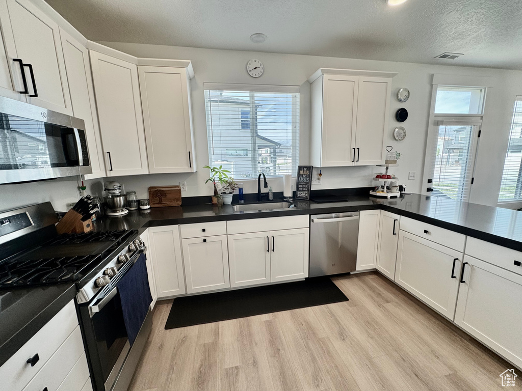 Kitchen featuring appliances with stainless steel finishes, light wood-style floors, white cabinets, dark countertops, and a textured ceiling