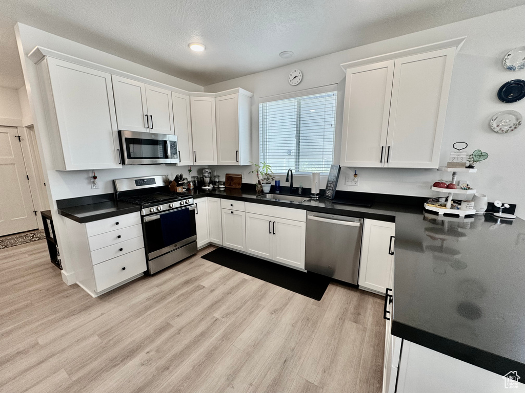 Kitchen with appliances with stainless steel finishes, white cabinetry, light wood finished floors, dark countertops, and a textured ceiling