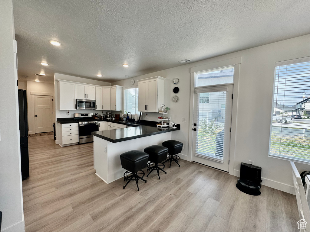 Kitchen featuring appliances with stainless steel finishes, light wood-style flooring, a textured ceiling, white cabinetry, and dark countertops