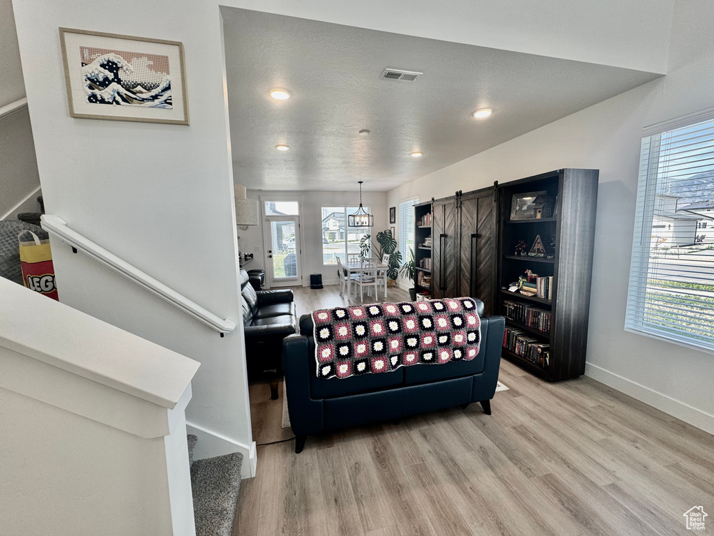 Living area featuring stairs, light wood-style flooring, a barn door, plenty of natural light, and recessed lighting