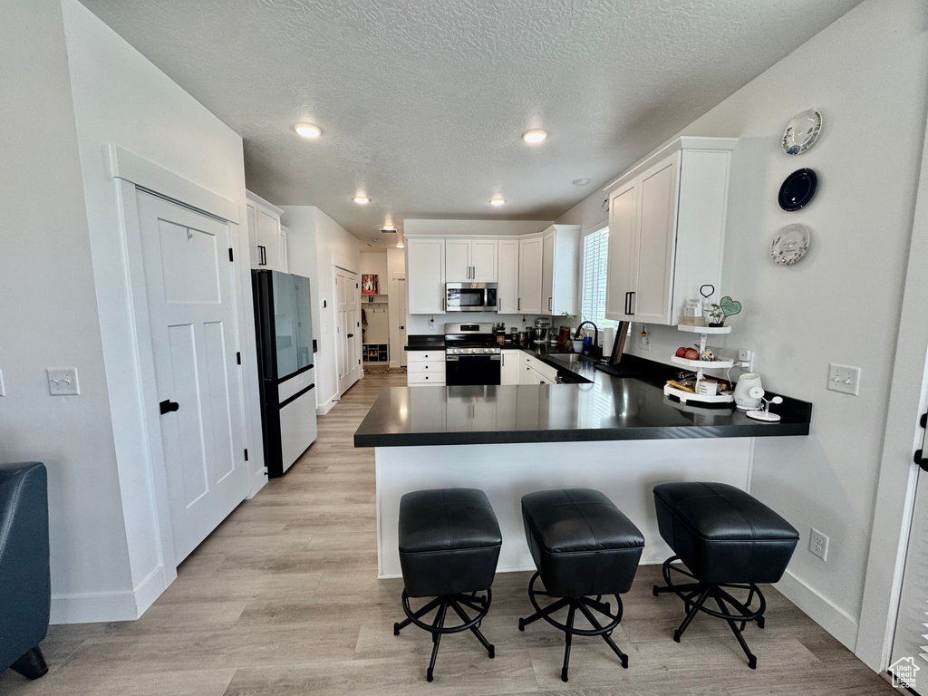 Kitchen featuring stainless steel appliances, dark countertops, a peninsula, a kitchen breakfast bar, and white cabinets