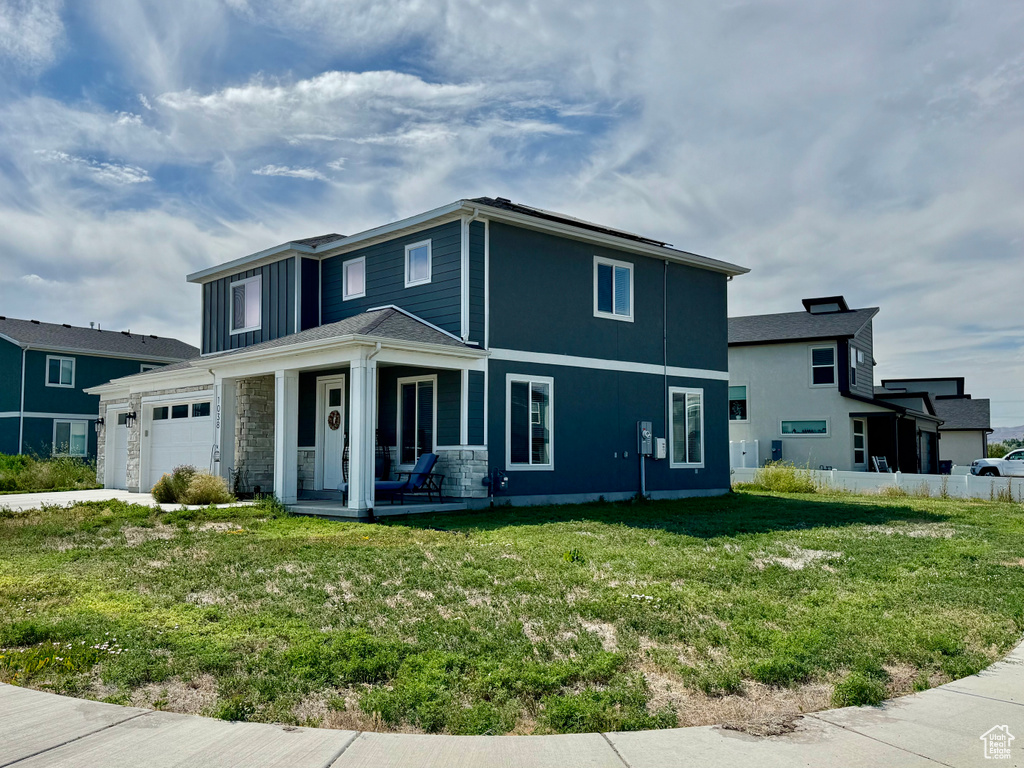 View of front of home with covered porch, a front lawn, and an attached garage