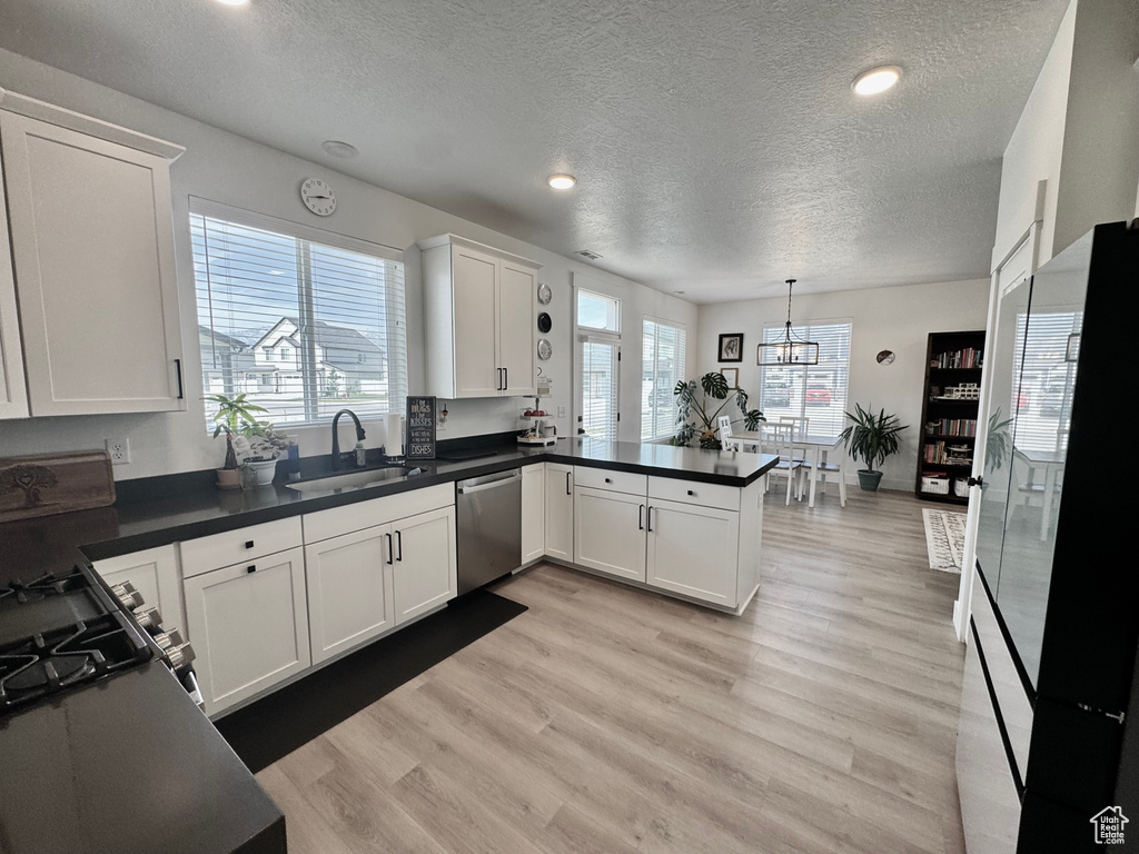 Kitchen with dishwasher, a textured ceiling, white cabinets, freestanding refrigerator, and light wood finished floors