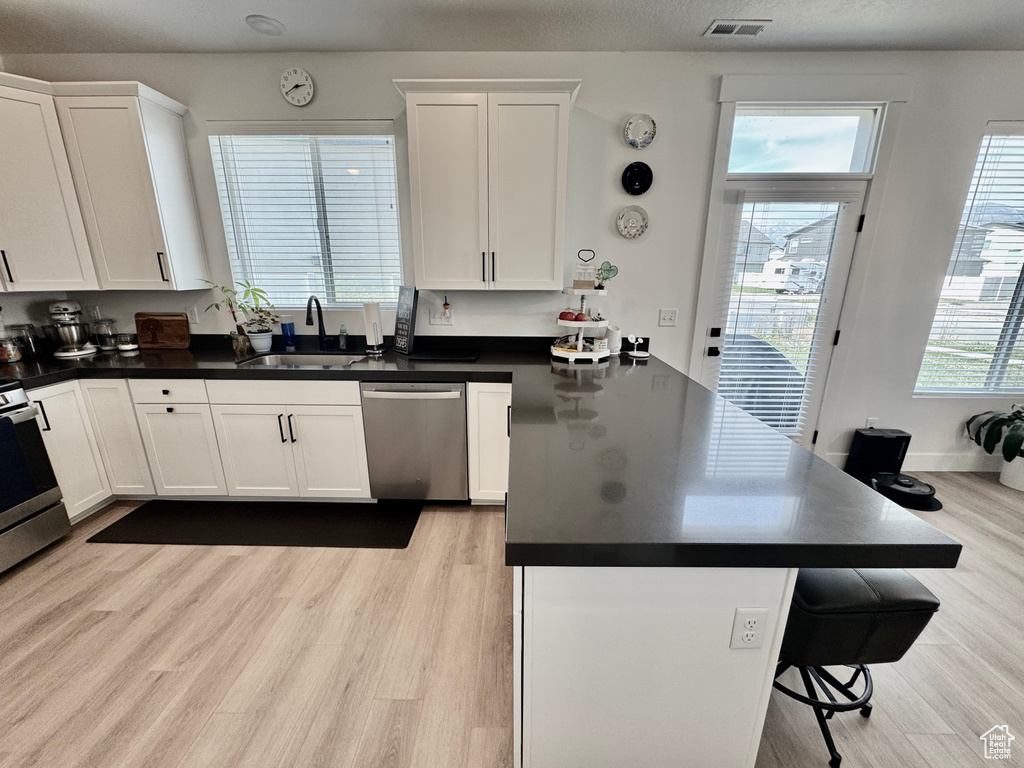 Kitchen with stainless steel appliances, a peninsula, light wood-style floors, and white cabinets