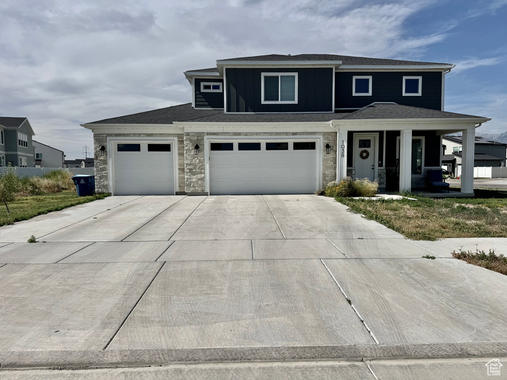 View of front of property featuring a porch, stone siding, driveway, and an attached garage