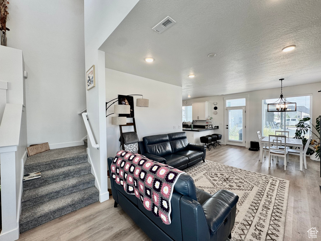 Living area featuring a chandelier, stairway, light wood-style flooring, a textured ceiling, and recessed lighting