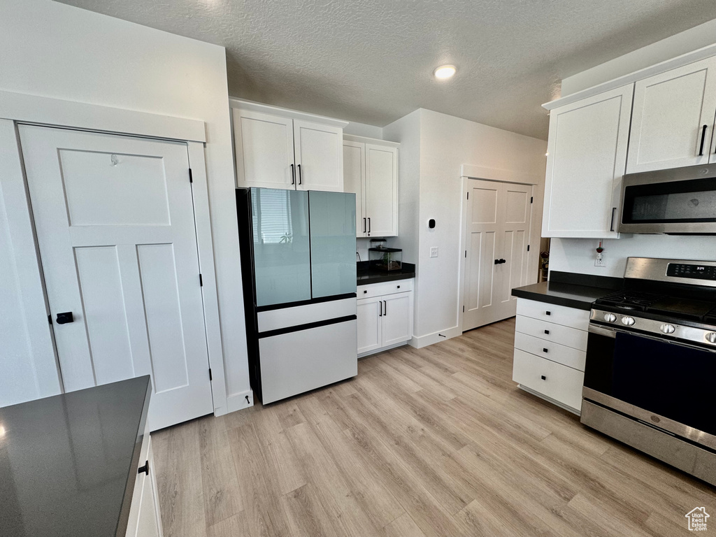 Kitchen with stainless steel appliances, dark countertops, light wood-type flooring, white cabinets, and a textured ceiling