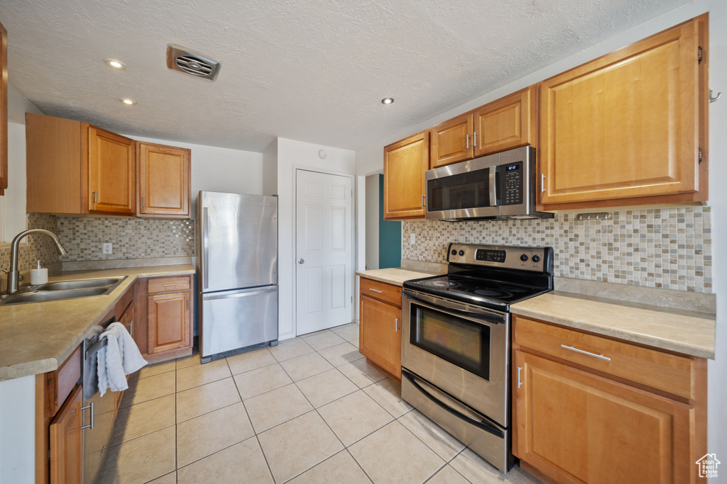 Kitchen with appliances with stainless steel finishes, light tile patterned floors, decorative backsplash, light countertops, and recessed lighting