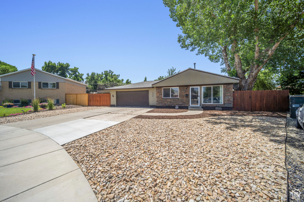Single story home featuring concrete driveway, an attached garage, and stone siding