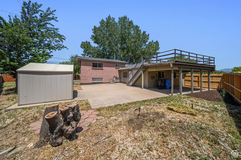Back of property with stairway, a patio area, a fenced backyard, a wooden deck, and a shed