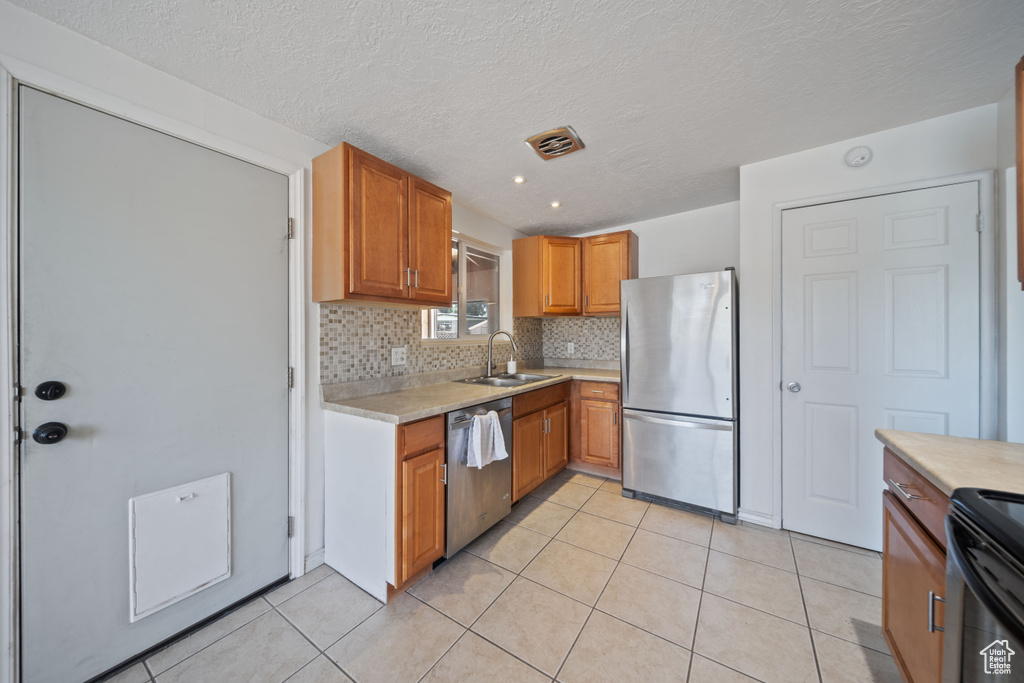 Kitchen featuring stainless steel appliances, light countertops, decorative backsplash, light tile patterned floors, and brown cabinets