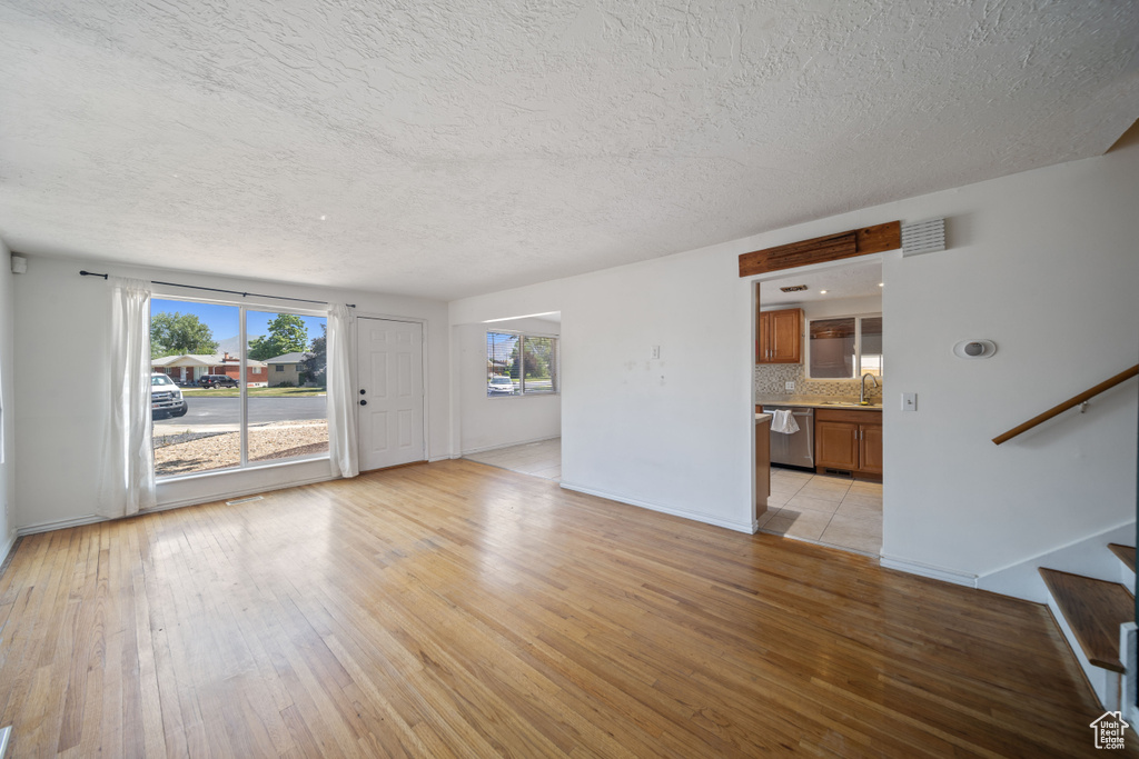 Unfurnished living room with light wood-type flooring, stairway, and a textured ceiling